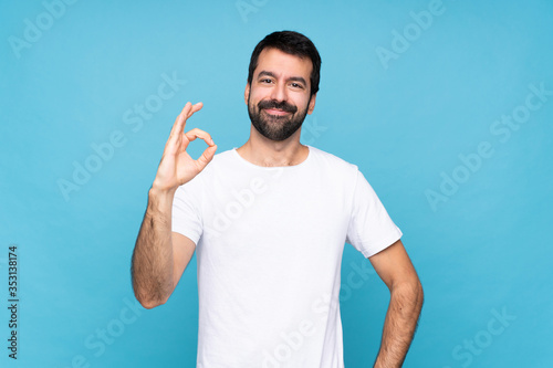 Young man with beard over isolated blue background showing ok sign with fingers