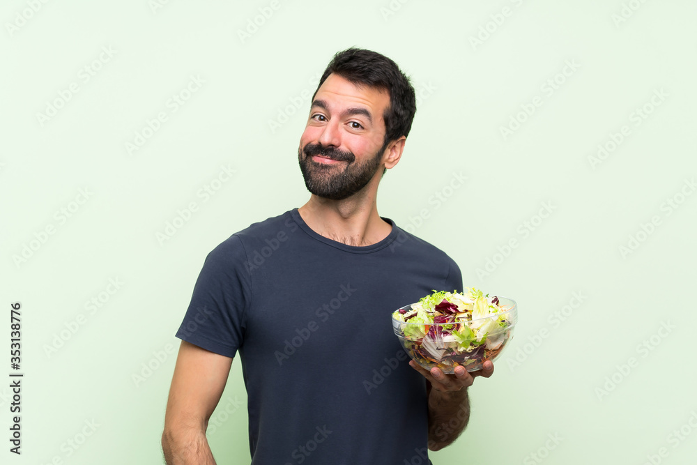 Young handsome man with salad over isolated green wall laughing Young handsome man with salad over isolated green wall laughing