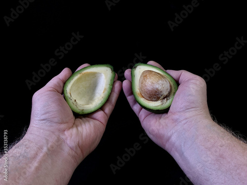 Halved avocado with a bone in his hand, on a black background. Green, ripe avocado vegetable in a cut. Persea