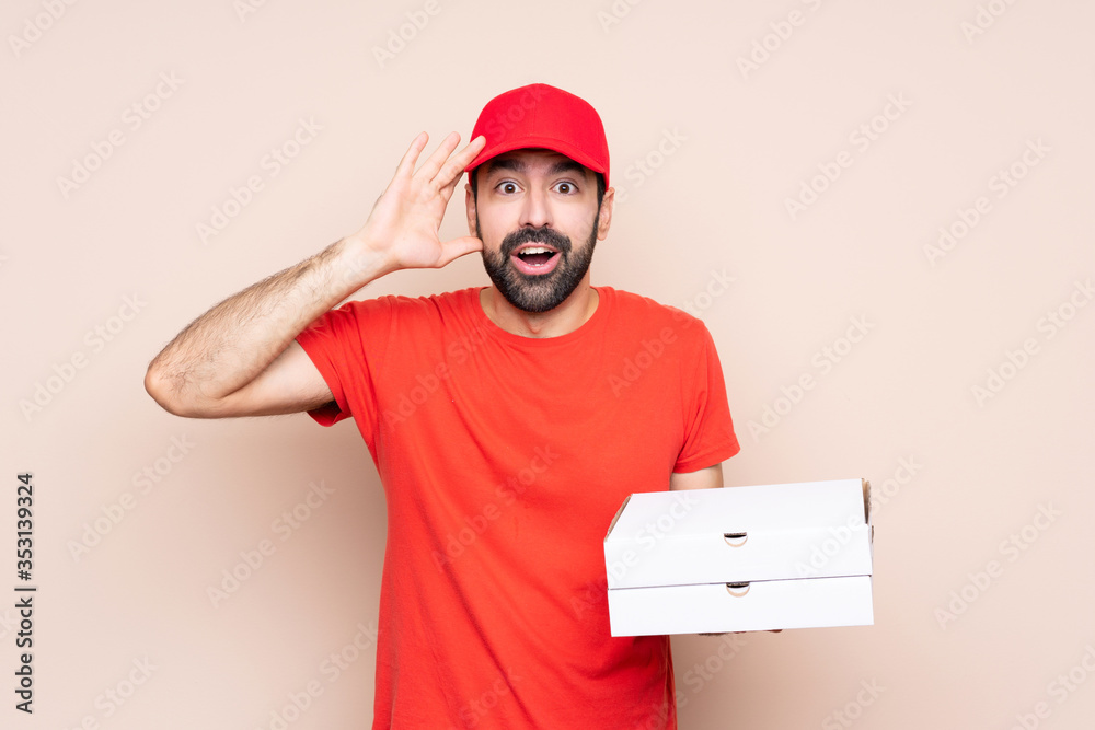 Young man holding a pizza over isolated background with surprise expression Young man holding a pizza over isolated background with surprise expression