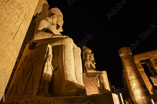 Statue and hieroglyphic carvings at an ancient egyptian temple in night