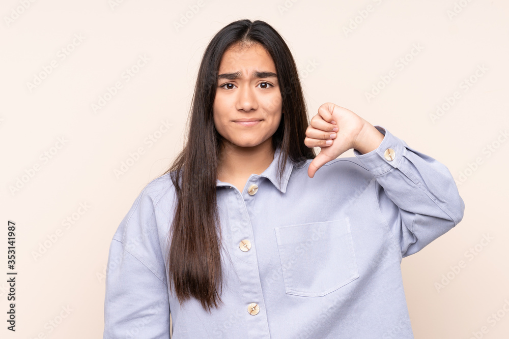 Young Indian woman isolated on beige background showing thumb down with negative expression Young Indian woman isolated on beige background showing thumb down with negative expression