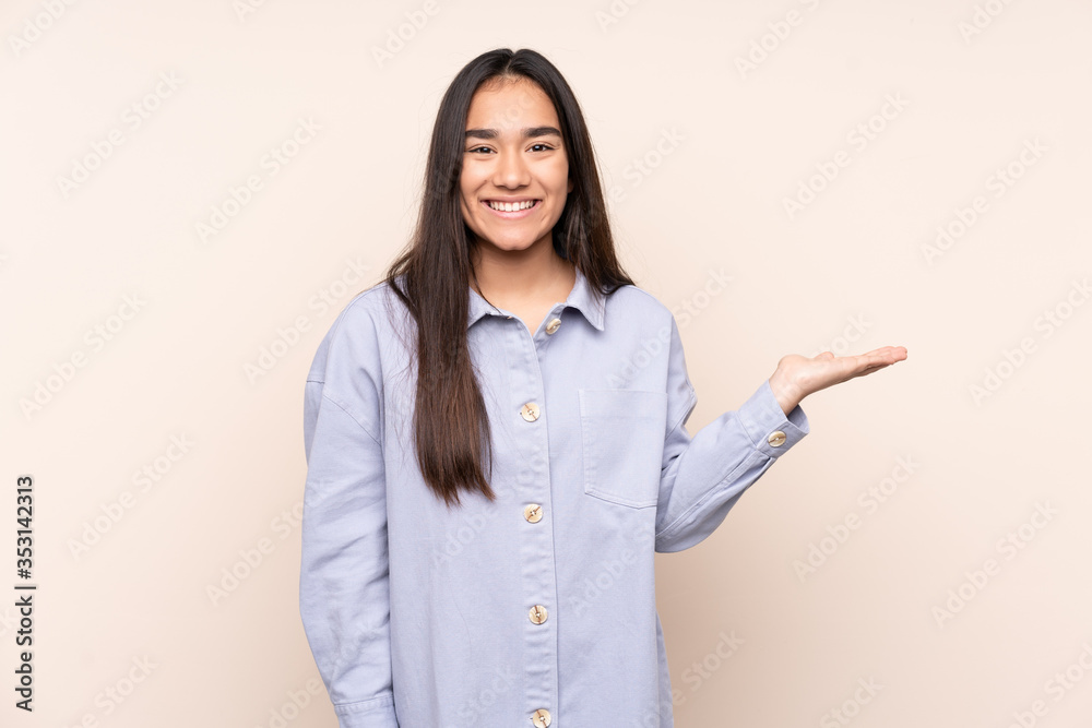 Young Indian woman isolated on beige background holding copyspace imaginary on the palm to insert an ad