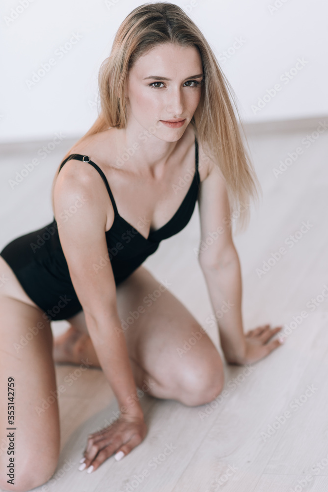 Blonde in a black swimsuit with long hair posing in the studio on a white background. Dressed in a white jacket and a straw hat Blonde in a black swimsuit with long hair posing in the studio on a white background. Dressed in a white jacket and a straw hat