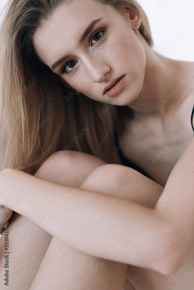 Blonde in a black swimsuit with long hair posing in the studio on a white background. Dressed in a white jacket and a straw hat Blonde in a black swimsuit with long hair posing in the studio on a white background. Dressed in a white jacket and a straw hat