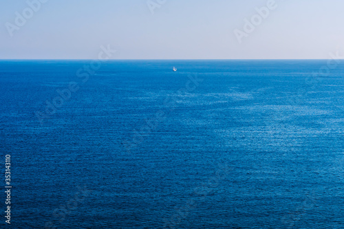 The surface of the sea is photographed from above. Aerial view of the azure wavy surface of sea water. A small sailing vessel far from the shore.