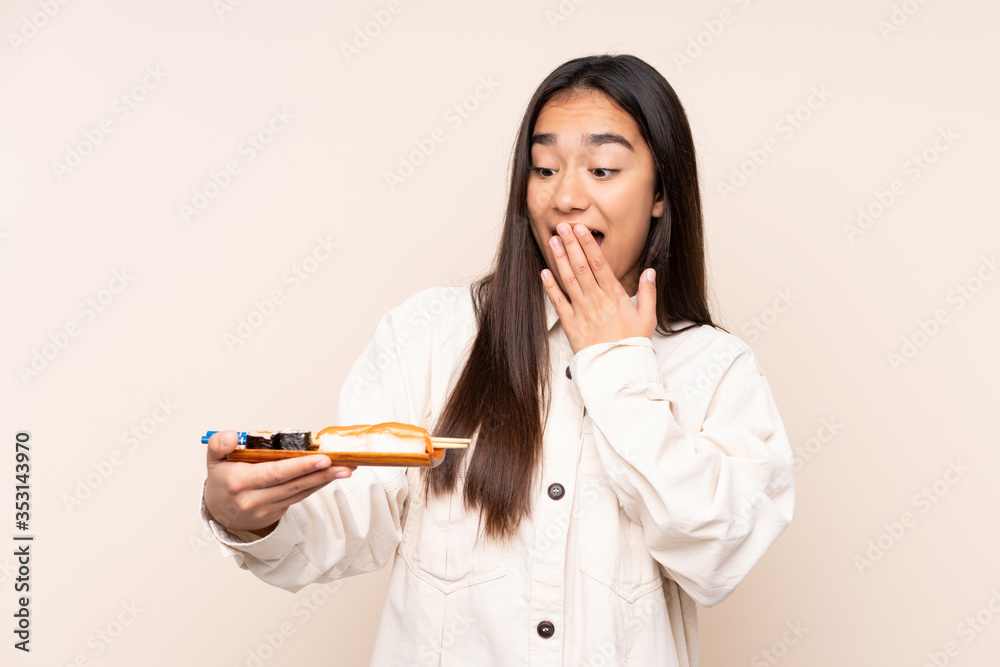 Young Indian woman holding sushi isolated on beige background with surprise and shocked facial expression Young Indian woman holding sushi isolated on beige background with surprise and shocked facial expression