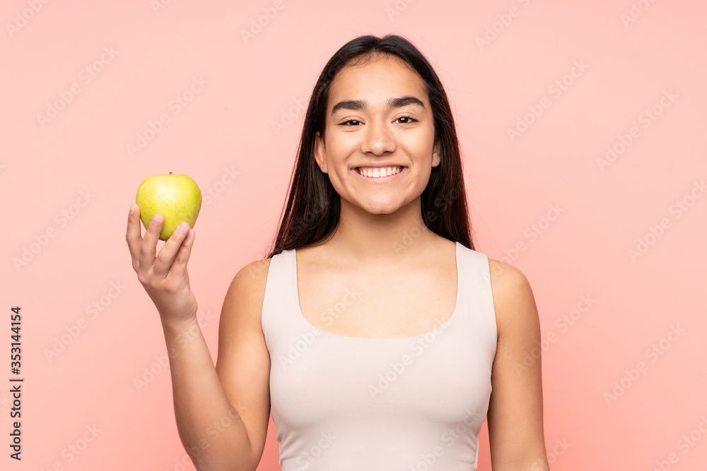 Young Indian woman isolated on pink background with an apple and happy Young Indian woman isolated on pink background with an apple and happy