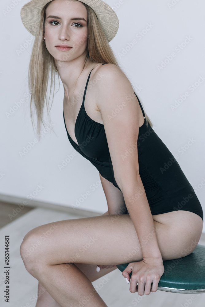 Blonde in a black swimsuit with long hair posing in the studio on a white background. Dressed in a white jacket and a straw hat Blonde in a black swimsuit with long hair posing in the studio on a white background. Dressed in a white jacket and a straw hat