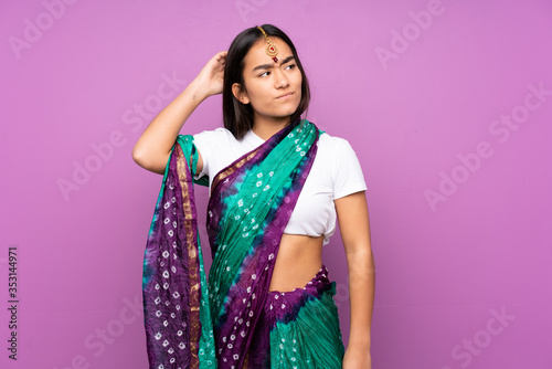 Young Indian woman with sari over isolated background having doubts while scratching head