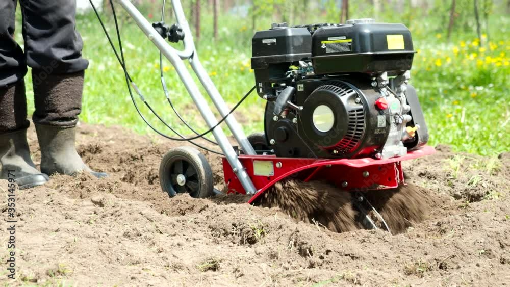 Man working with garden tiller engine in 4k VIDEO. Cultivator machine ploughing and shredding soil with blades on field at spring. Modern farming, technology agriculture. Close-up. Man working with garden tiller engine in 4k VIDEO. Cultivator machine ploughing and shredding soil with blades on field at spring. Modern farming, technology agriculture. Close-up.