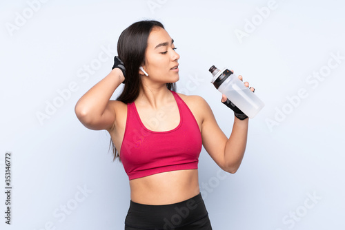 Young Indian sport woman isolated on blue background with sports water bottle