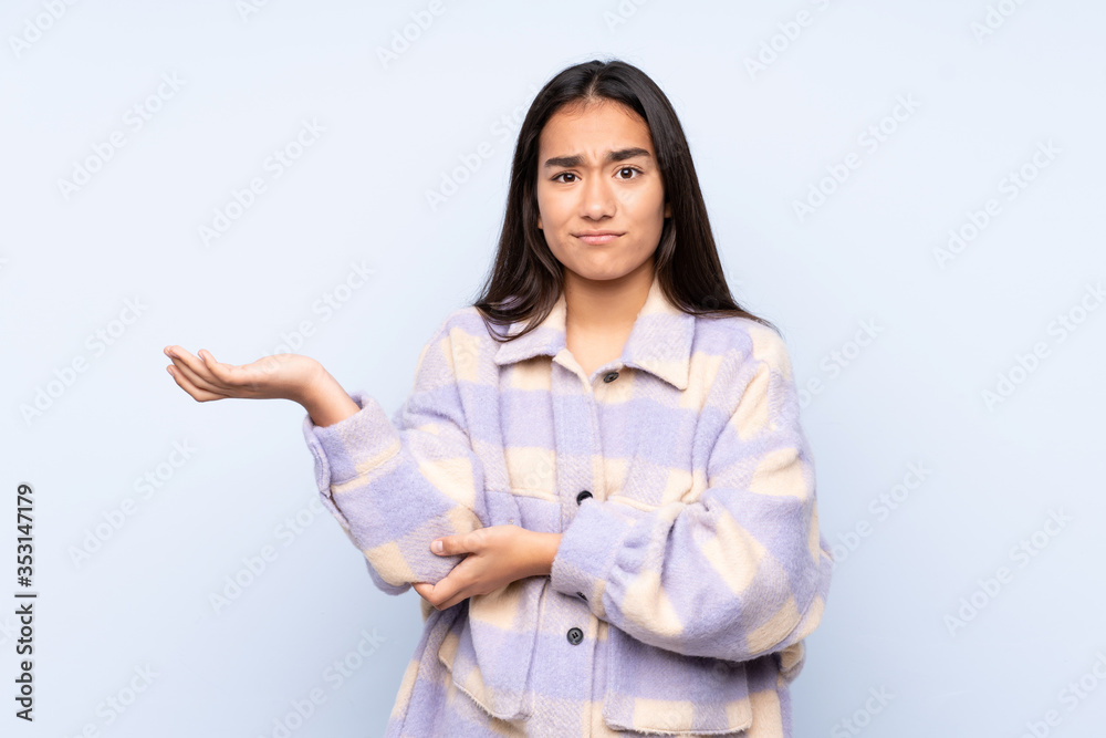 Young Indian woman isolated on blue background unhappy for not understand something Young Indian woman isolated on blue background unhappy for not understand something