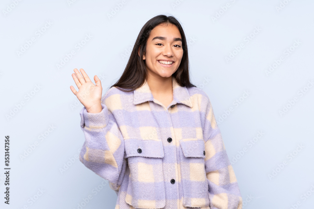 Young Indian woman isolated on blue background saluting with hand with happy expression