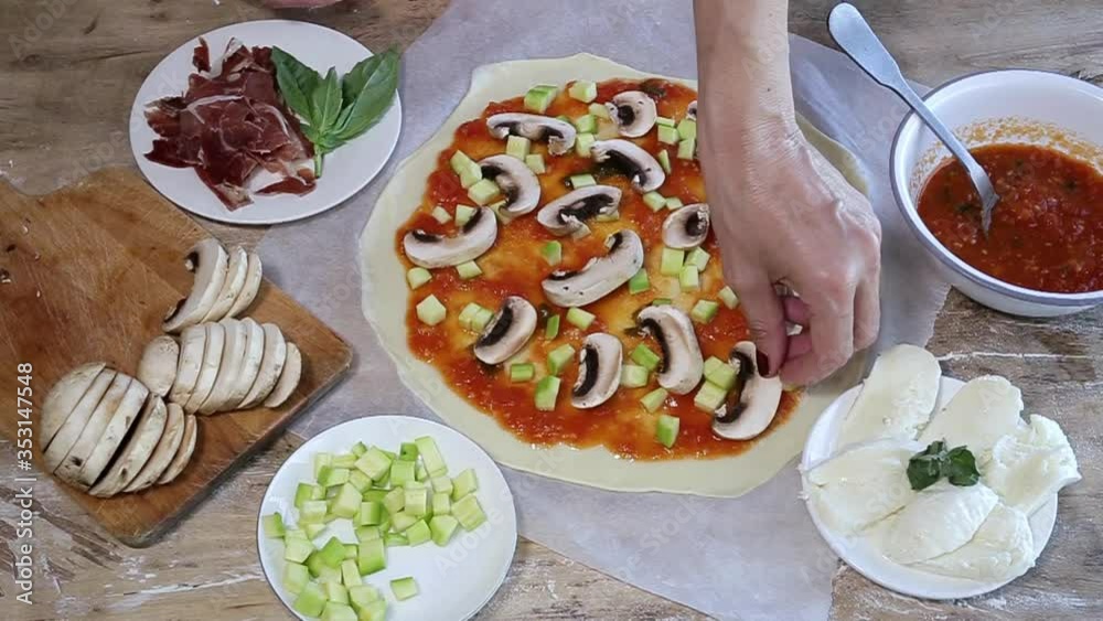Cook hands making pizza dough and preparing with tomato, mushrooms, ham, mozzarella and parmesan cheese.