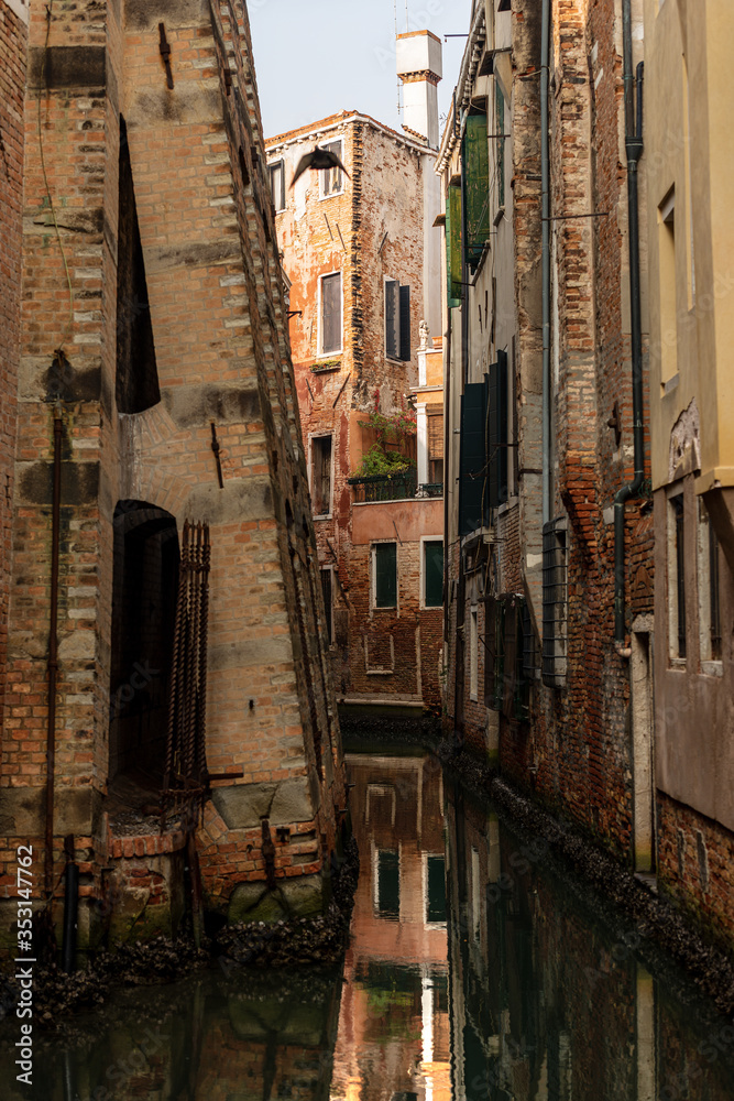 Venice, foreshortening of the city with a narrow canal of the lagoon and old houses. In the foreground the lower part of the bell tower of Santo Stefano church. Veneto, Italy, Europe