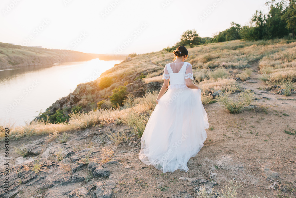 Bride in a luxurious white wedding dress in nature at sunset