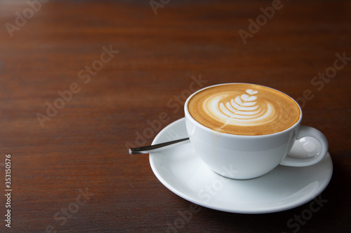Top-view shot with copy space of single cup of latte coffee with art cream foam in white ceramic cup on wooden vintage table with sun lighting and shade in the morning after breakfast for relaxing.
