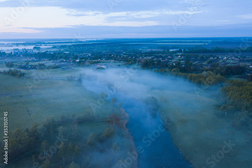 Calm cold river landscape with fog and blue clouds in the early morning near the village. Aerial shot. 