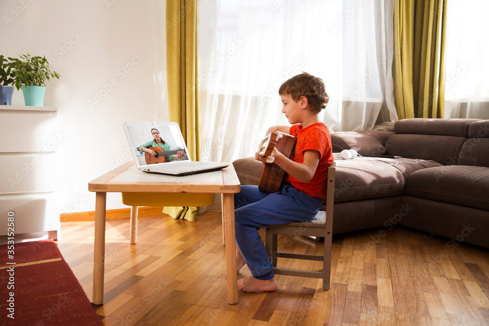 Kid boy playing guitar and watching online lessons on laptop while practicing at home. Stay home. quarantine. Online training, online classes.
Kid boy playing guitar and watching online lessons on laptop while practicing at home. Stay home. quarantine. Online training, online classes.