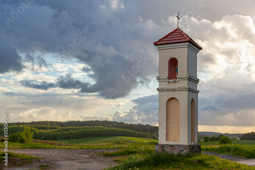 Kapliczka polna w Gietrzwałdzie - wieś na Warmii i mazurach, Polska - krajobraz wiosenny, padający deszcz, zachód słońca.