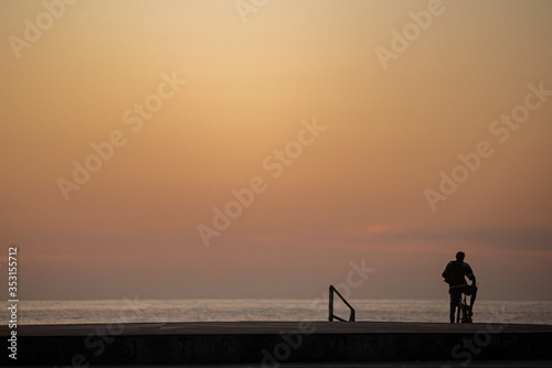 A man on his bicycle watches the sunrise on the beach.