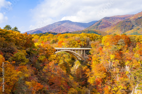 View of a bridge in crossing the Naruko Gorge near Sendai, Miyagi, Japan with trees with autumn color maple leaves all over the mountain in a sunny day photo