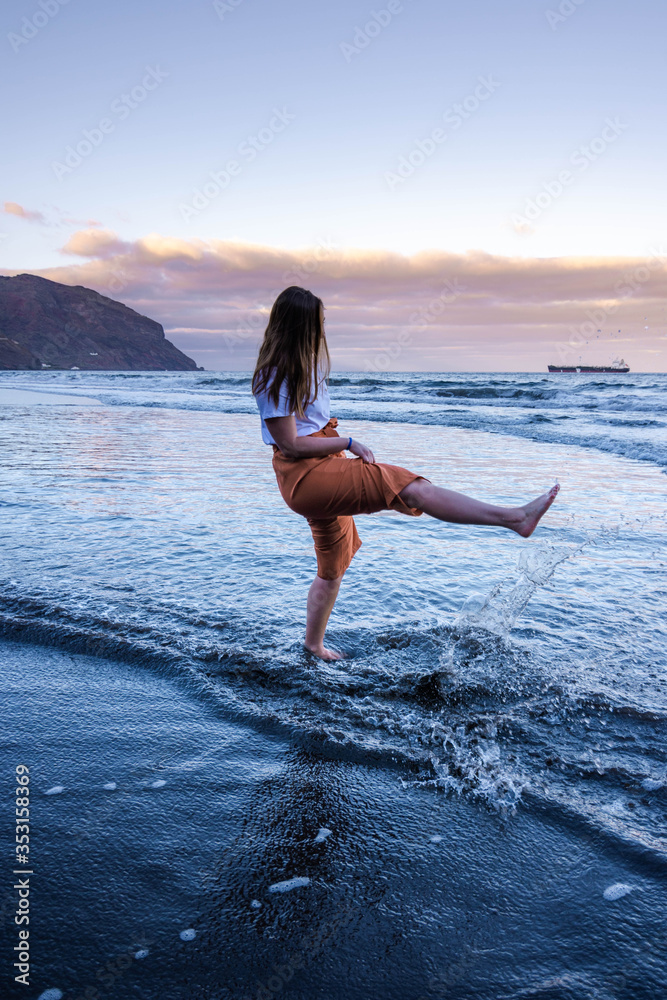 Woman playing on the shore with the water of a black sand beach at sunset Woman playing on the shore with the water of a black sand beach at sunset