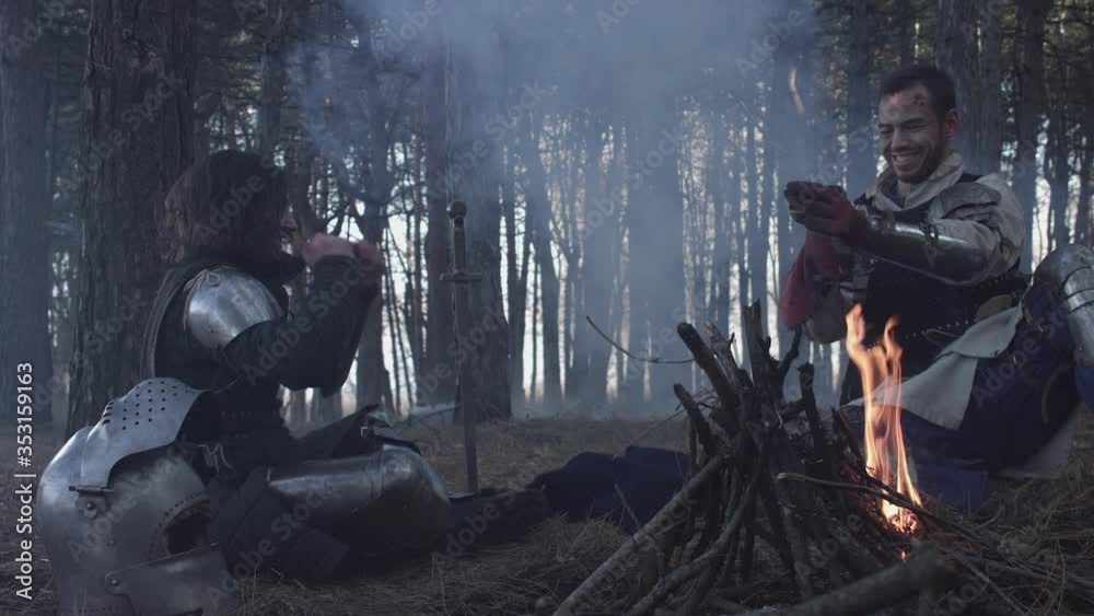 Two medieval knights sitting near bonfire and devide production Two medieval knights sitting near bonfire and devide production