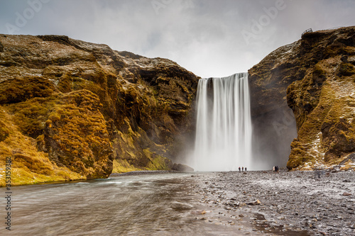 Skogafoss waterfall in South Iceland. Tourists admiring the waterfall. Popular and famous tourist attraction.