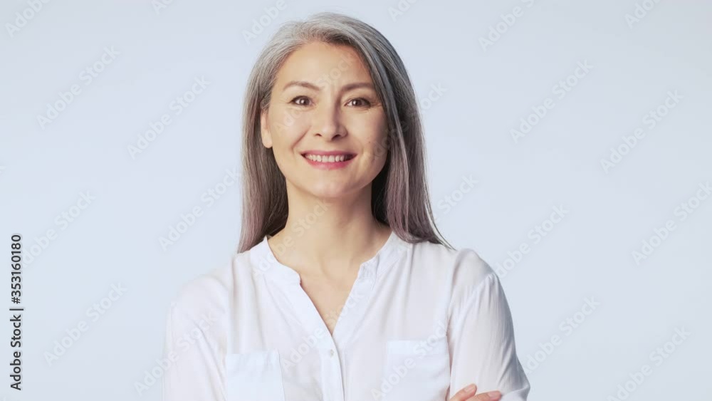 A friendly pleased old mature woman with long gray hair wearing formal business clothes is smiling standing isolated over white background in studio A friendly pleased old mature woman with long gray hair wearing formal business clothes is smiling standing isolated over white background in studio