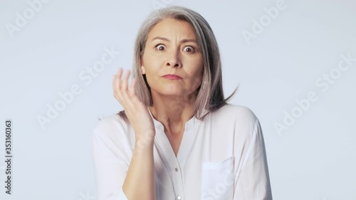 A serious confused old mature woman with long gray hair wearing formal business clothes is thinking about something isolated over white background in studio