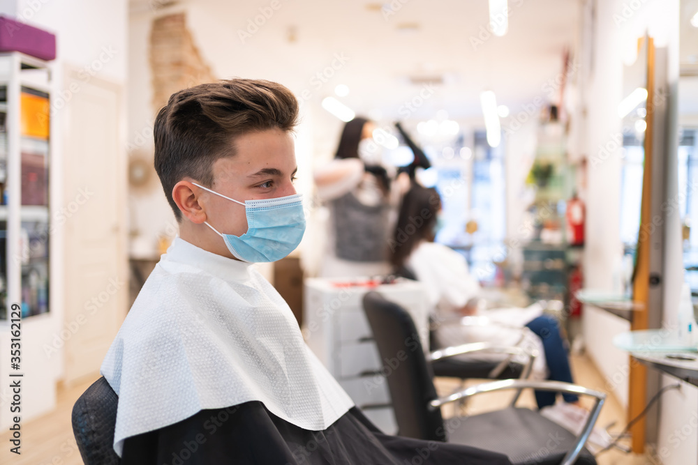 Profile portrait of a boy with a protective mask sitting on a chair in a hairdressing salon
