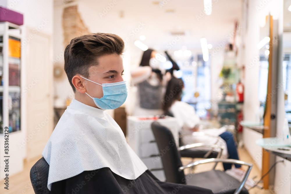Profile portrait of a boy with a protective mask sitting on a chair in a hairdressing salon Profile portrait of a boy with a protective mask sitting on a chair in a hairdressing salon