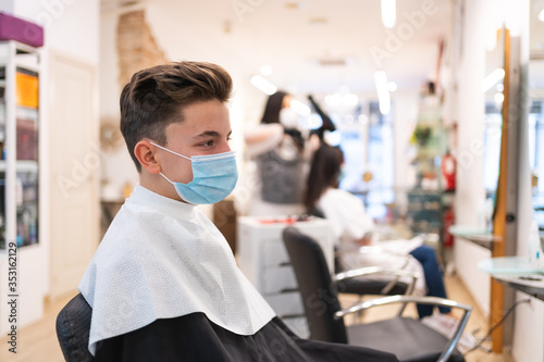 Profile portrait of a boy with a protective mask sitting on a chair in a hairdressing salon