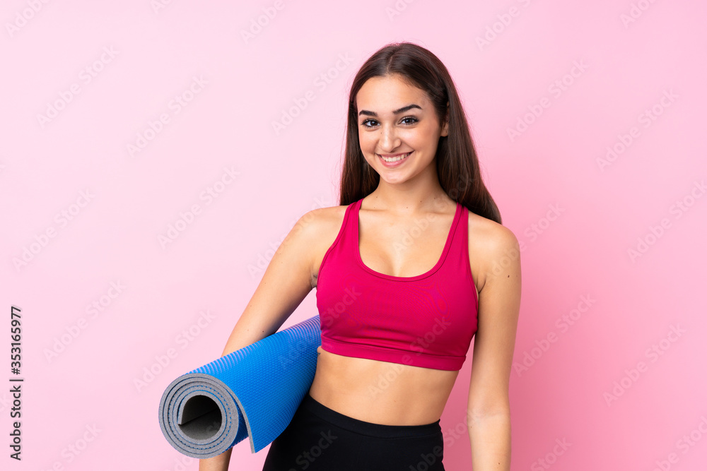 Young sport girl over isolated pink background with a mat and smiling Young sport girl over isolated pink background with a mat and smiling