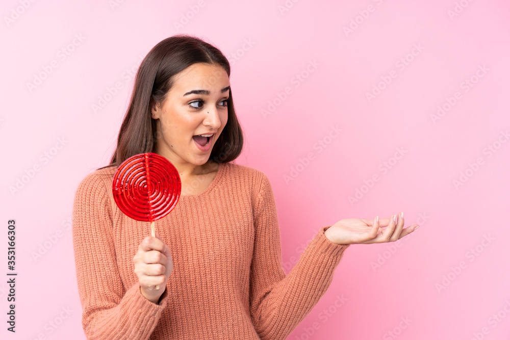 Young girl holding a lollipop over pink background with surprise facial expression Young girl holding a lollipop over pink background with surprise facial expression
