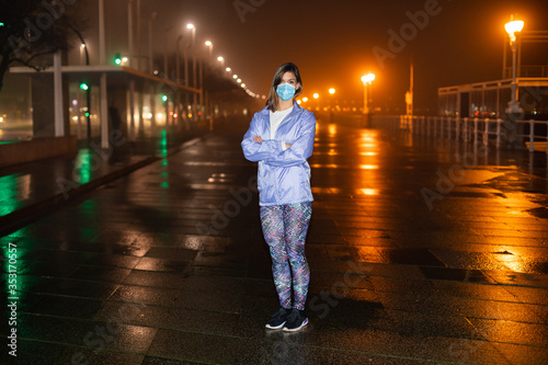 Condifent female athlete on urban night fitness and running workout wearing face mask against Covid-19. photo