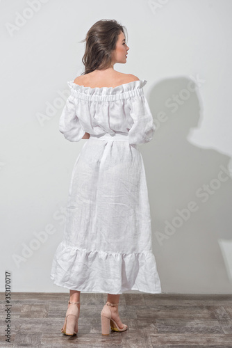 Back view of the pretty girl in a white dress over white wall