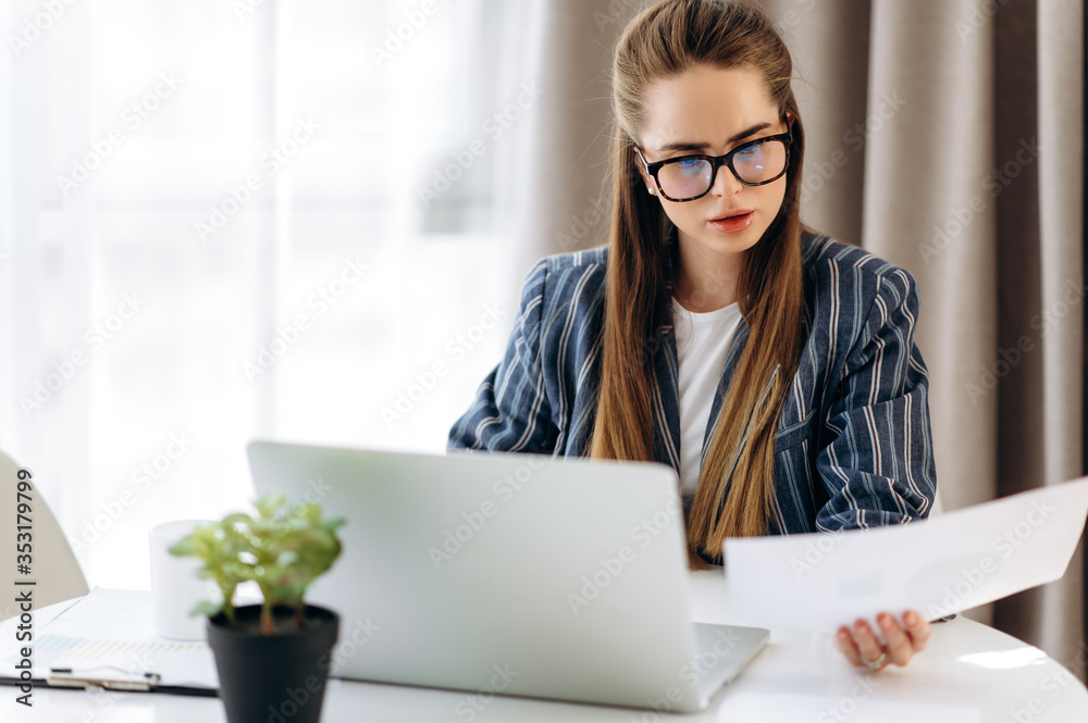 Attractive business woman in formal stylish clothes works in a laptop and analyzes charts and statistics while sitting at her workplace Attractive business woman in formal stylish clothes works in a laptop and analyzes charts and statistics while sitting at her workplace