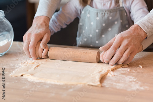 Father Helping To Little Daughter Roll The Dough On Kitchen Table