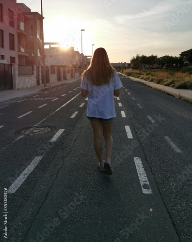 A young woman is walking into the sunset on a road