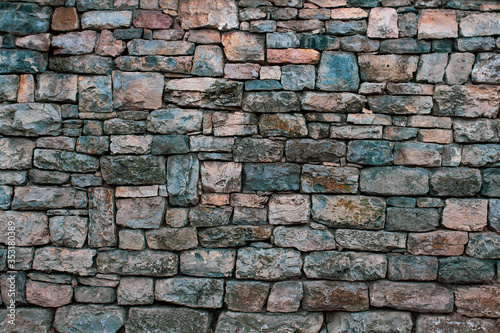 Background in the form of a granite stone wall with a fallen solution and different sizes of stones. The old colored bricks are faded and gray with age.