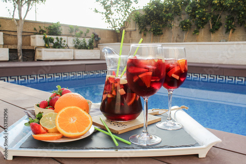 Spanish red wine (Sangria) with fruit. Strawberry, orange, Apple and banana slices. On a tray next to the pool