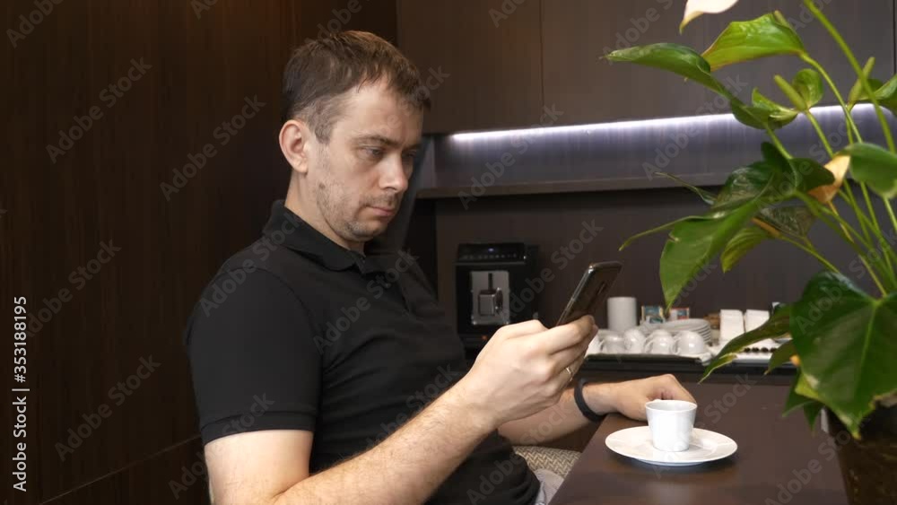 Man Sitting in Coffee Shop and Using His Mobile Phone, Watching the News and Checking Social Media Man Sitting in Coffee Shop and Using His Mobile Phone, Watching the News and Checking Social Media
