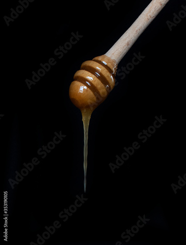 Hand holding honey stick.  Dripping honey on black background.