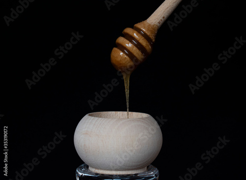 Wooden jar full of honey and dripping honey stick on black background