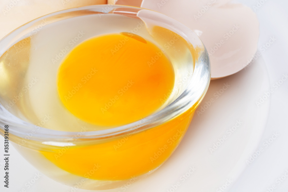 Image of yolk and squirrel in a transparent round cup on a plate. Egg in a transparent cup on a plate. Closeup