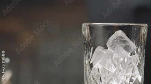 Making a Long Island Ice Tea Cocktail. Close up bartenders hands throwing ice cubes into a glass, pouring strong alcohol and cold tea and putting a piece of lemon. Crystal glass moving on a slider