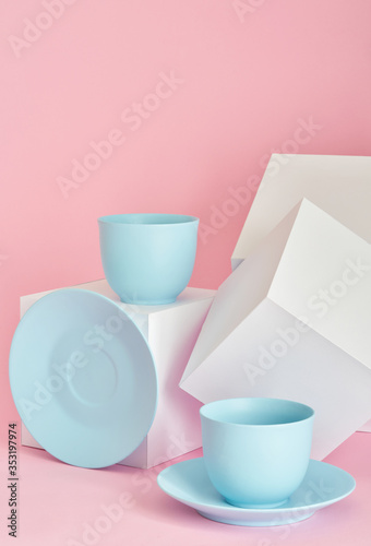 minimalism concept with light pastel colored blue cups and plate with white paper cubs on pink background.